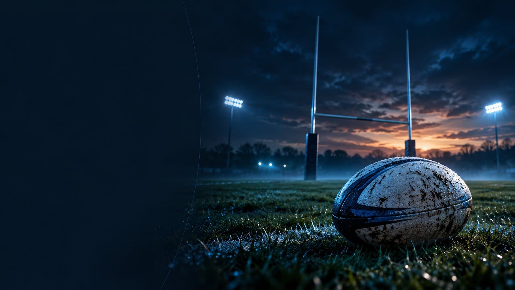 A rugby ball on a floodlit pitch at dusk, with rugby posts against an orange sky